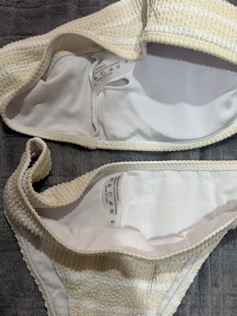 Striped Smocked Bikini Set Size S (Category: Bikinis & Swimsuits) located in Bulacan. Submitted by richelleregala (Listing ID 1468079284, Image 2). Description: - Condition: Brand new, never worn with tags attached - Size: Small (fits both top and bottom) - Color/Pattern: Light cream and white stripes - Material: 95% polyester, 5% elastane (textured crinkle fabric, fully lined) - Top: Bandeau style with trendy tortoiseshell square ring buckle - B