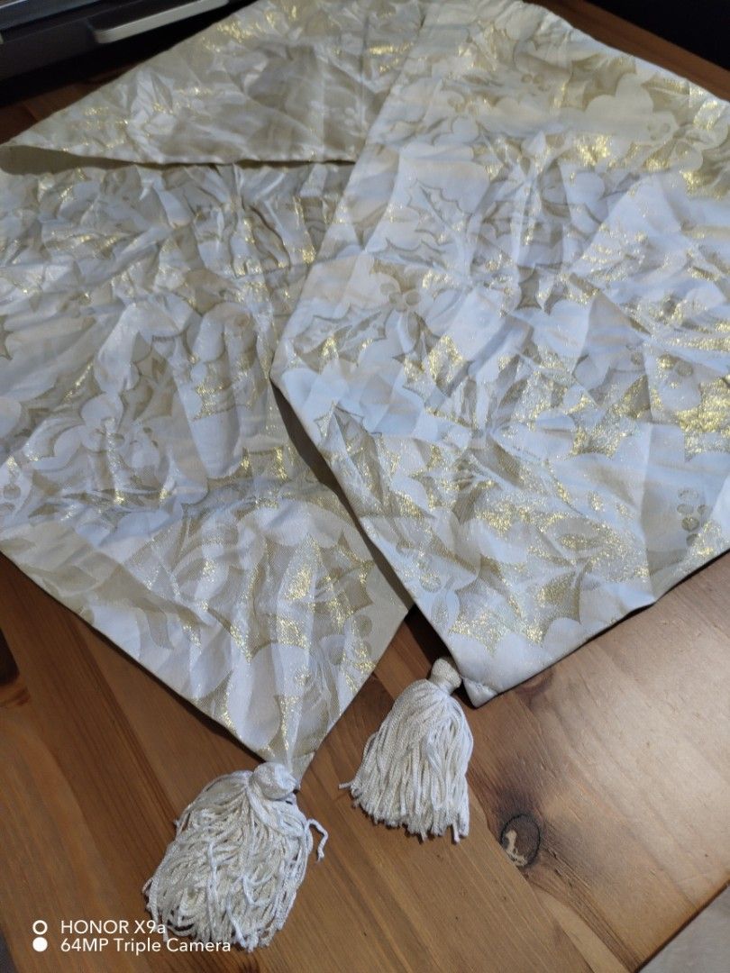 Table Runner (Category: Towels, Napkins & Holders) located in Muntinlupa City. Submitted by arciagamaryann68 (Listing ID 1468107193, Image 2). Description: - Color: White with metallic gold details - Design: Festive holly leaf pattern - Feature: Elegant hanging tassels on both ends - Ideal for: Dining tables, holiday parties, and home decor - Condition: Good pre-owned/ready-to-use condition.