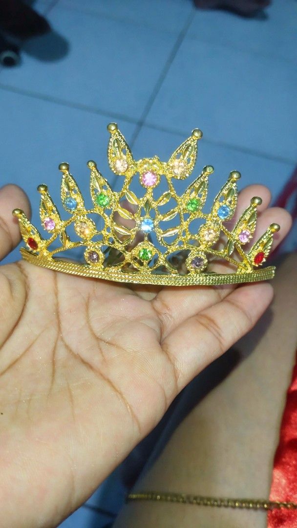 Thai crown gold (Category: Hair Accessories) located in Valenzuela. Submitted by diane.35 (Listing ID 1468102570, Image 1). Description: - Design: Gold tone miniature crown hair comb - Embellishments: Colorful rhinestones in blue, pink, green, orange, and purple - Features: Built-in comb prongs on the back for a secure hold - Styling: Great for updos, ponytails, and half-up hairstyles - Occasions: Fun accessory for parties, costumes, or daily wea
