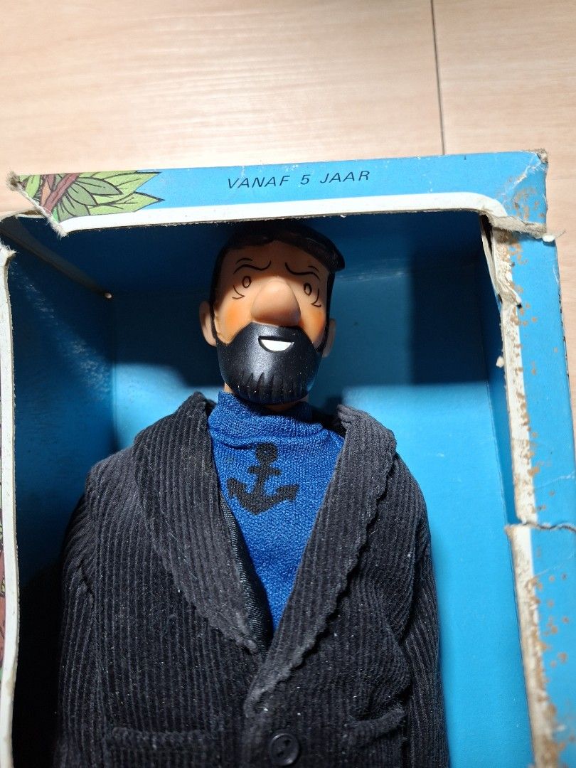 Tintin Captain Haddock doll in original box (Category: Figurines & Statues) located in Baguio. Submitted by restyrille77846 (Listing ID 1468204053, Image 2). Description: - Vintage Captain Haddock collectible figure from The Adventures of Tintin - Wears his signature blue sweater with anchor logo, black jacket, and dark trousers - Comes in an original illustrated cardboard box with a clear cutout display window - Features unique Dutch text on the
