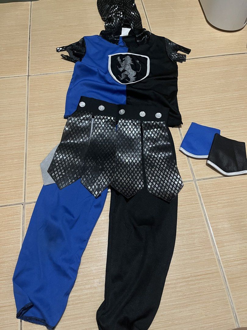Toddler Knight Costume (Category: Babies & Kids Fashion) located in Quezon City. Submitted by lovedbykarlaa (Listing ID 1468067703, Image 2). Description: - Size: S (fits toddlers 92 to 104cm in height) - Color: Blue and black - Complete Set: Includes shirt with attached hood, pants, belt, and arm guards - Design Details: Features a cool lion crest shield emblem on the chest and stylish mesh fabric on the sleeves and skirt overlay - Condition: Co