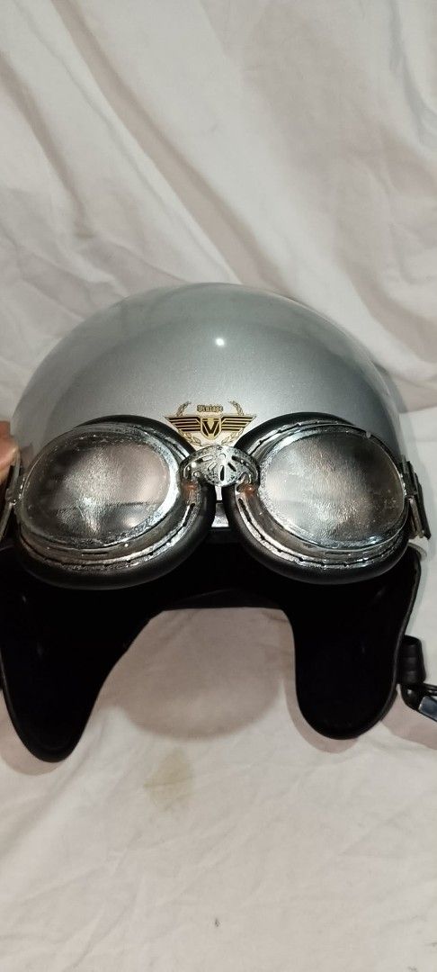 Vintage Silver Motorcycle Helmet With Goggles (Category: Bicycles) located in Quezon City. Submitted by jpnvintageonline (Listing ID 1468236639, Image 1). Description: - Style: Classic retro half-face design with glossy silver finish - Extras: Includes attached silver-framed riding goggles with dark padding - Branding: Features a stylish gold and black 'Vintage' wing emblem on the front - Comfort & Fit: Comfortable black interior lining and secur