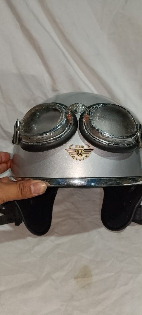 Vintage Silver Motorcycle Helmet With Goggles (Category: Bicycles) located in Quezon City. Submitted by jpnvintageonline (Listing ID 1468236639, Image 3). Description: - Style: Classic retro half-face design with glossy silver finish - Extras: Includes attached silver-framed riding goggles with dark padding - Branding: Features a stylish gold and black 'Vintage' wing emblem on the front - Comfort & Fit: Comfortable black interior lining and secur