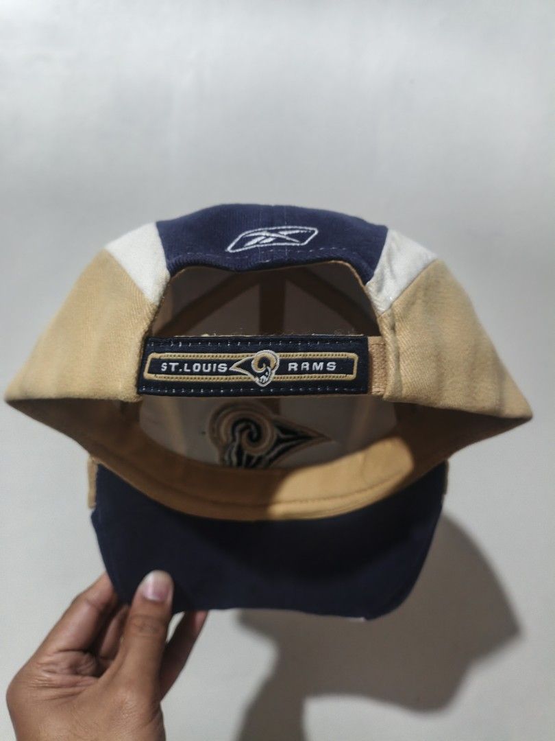 Vintage St. Louis Rams Reebok NFL Cap Hat (Category: Caps & Hats) located in San Jose. Submitted by ezsenthrift475 (Listing ID 1468233664, Image 2). Description: - Vintage St. Louis Rams cap by Reebok - Classic blue, gold, and white colorblock design - Embroidered team logo on the front - 'NFC West' text embroidered on the brim - Adjustable strapback closure with 'ST. LOUIS RAMS' detail - Official NFL interior tag.