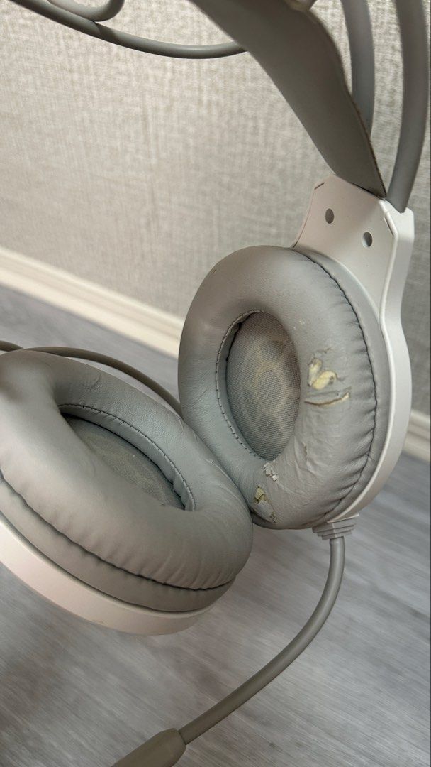 White gaming headset with mic and wired connectors (Category: Headphones & Headsets) located in Makati City. Submitted by glyzacatalan (Listing ID 1468084986, Image 3). Description: - White over-ear gaming headset with built-in microphone - 100% fully functional for PC gaming and audio listening - Wired setup with connected dual 3.5mm audio jacks and USB plug - Cosmetic flaw: Noticeable peeling and wear on the synthetic leather ear cushions and h