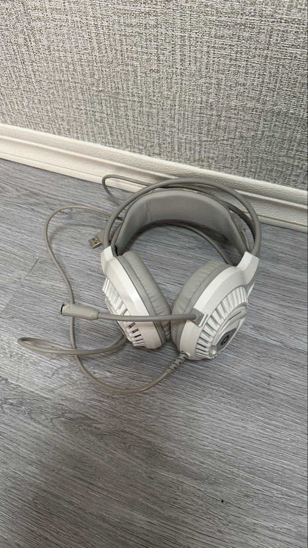 White gaming headset with mic and wired connectors (Category: Headphones & Headsets) located in Makati City. Submitted by glyzacatalan (Listing ID 1468084986, Image 1). Description: - White over-ear gaming headset with built-in microphone - 100% fully functional for PC gaming and audio listening - Wired setup with connected dual 3.5mm audio jacks and USB plug - Cosmetic flaw: Noticeable peeling and wear on the synthetic leather ear cushions and h