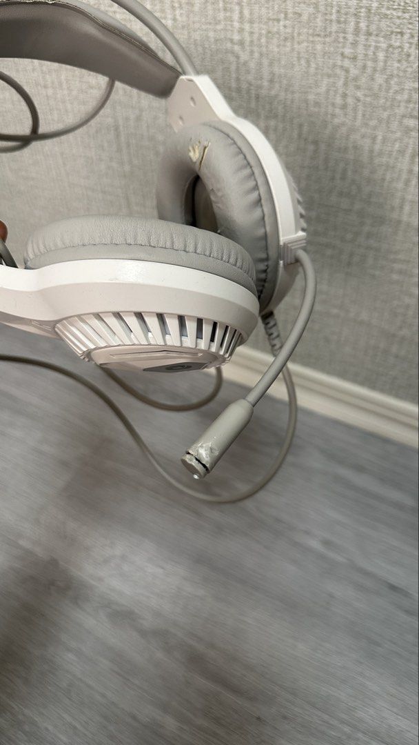 White gaming headset with mic and wired connectors (Category: Headphones & Headsets) located in Makati City. Submitted by glyzacatalan (Listing ID 1468084986, Image 2). Description: - White over-ear gaming headset with built-in microphone - 100% fully functional for PC gaming and audio listening - Wired setup with connected dual 3.5mm audio jacks and USB plug - Cosmetic flaw: Noticeable peeling and wear on the synthetic leather ear cushions and h