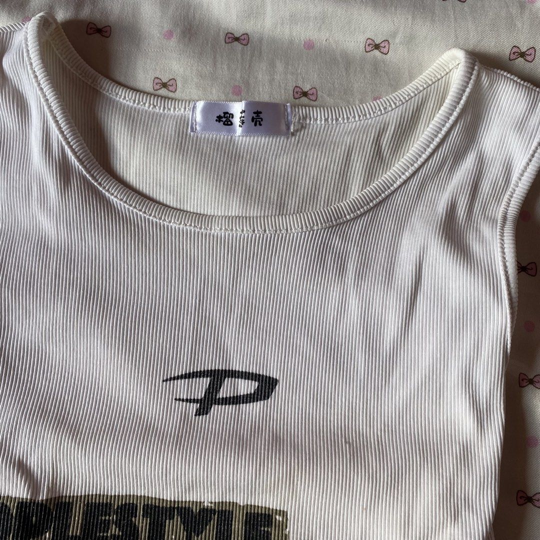 White ribbed graphic tank top with text print (Category: Sleeveless) located in Santiago. Submitted by dear_darlingdoll (Listing ID 1468127803, Image 3). Description: White ribbed tank top with graphic text prints and distressed patches. Scoop neckline and sleeveless cut. Fitted style with a slight flare at the bottom hem. Brand tag attached at the inner collar. Material has good stretch..
