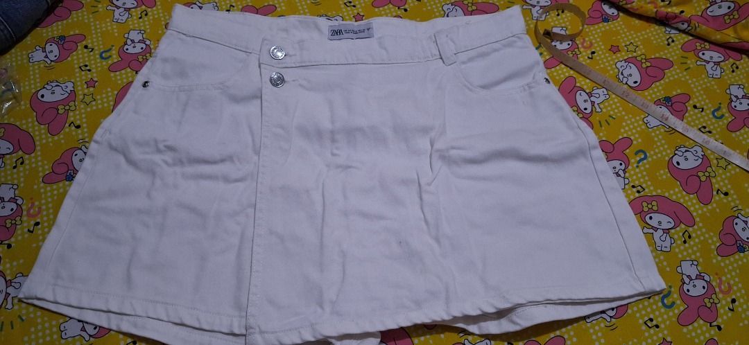 ZARA White Denim Skirt Size 38 (Category: Skirts) located in Manila. Submitted by katkween23 (Listing ID 1468079963, Image 1). Description: - Brand: ZARA - Style: White denim skirt with asymmetrical button front - Size: 38 on tag - Measurements: Waist approx. 16-17" across, Length approx. 16" - Features: Sturdy denim fabric, functional front pockets - Condition: Good, with a small faint stain near the right pocket area - Versatile, classic piece 