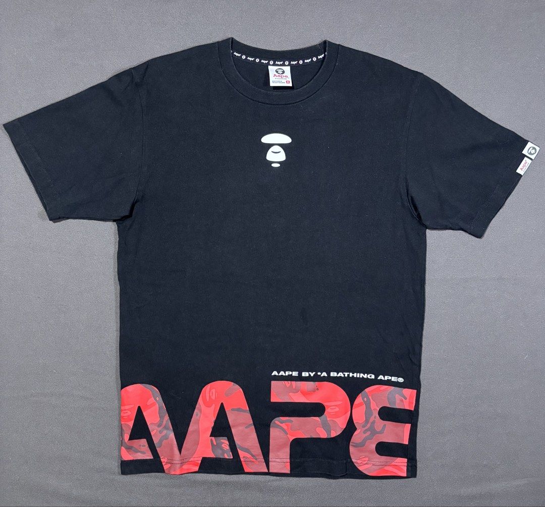 AAPE By A Bathing Ape (Category: Tshirts & Polo Shirts ) located in Mabalacat. Submitted by _limitlessfashion (Listing ID 1468291929, Image 1). Description: - Brand: AAPE by A Bathing Ape - Color: Black - Size: Medium - Length 27 - Width 20 - Color rate 9.5 or better - No major issue - Design: White Ape head logo on chest with striking red camo AAPE lettering across the bottom hem - Details: Upper back branding, interior branded neck taping, wove