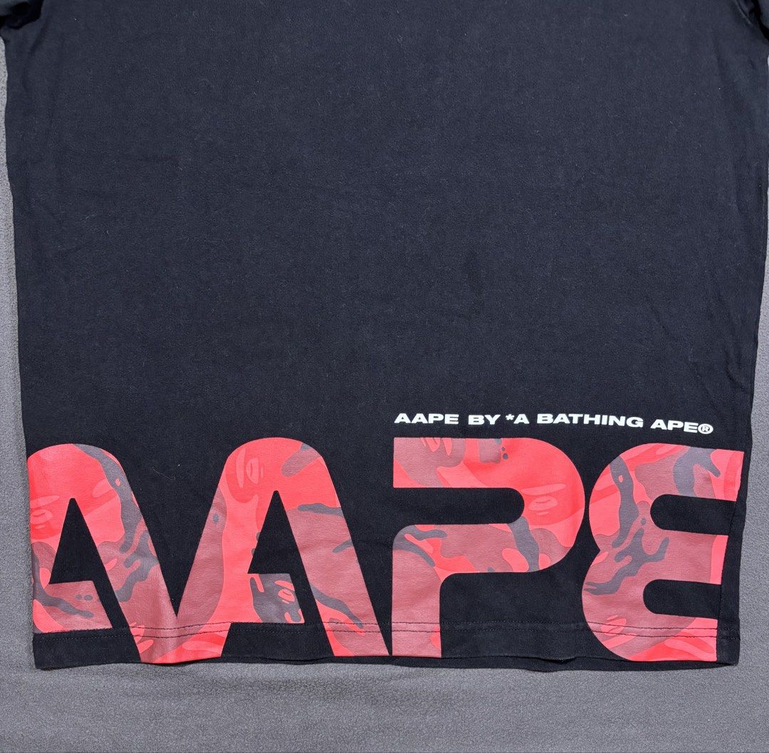 AAPE By A Bathing Ape (Category: Tshirts & Polo Shirts ) located in Mabalacat. Submitted by _limitlessfashion (Listing ID 1468291929, Image 2). Description: - Brand: AAPE by A Bathing Ape - Color: Black - Size: Medium - Length 27 - Width 20 - Color rate 9.5 or better - No major issue - Design: White Ape head logo on chest with striking red camo AAPE lettering across the bottom hem - Details: Upper back branding, interior branded neck taping, wove