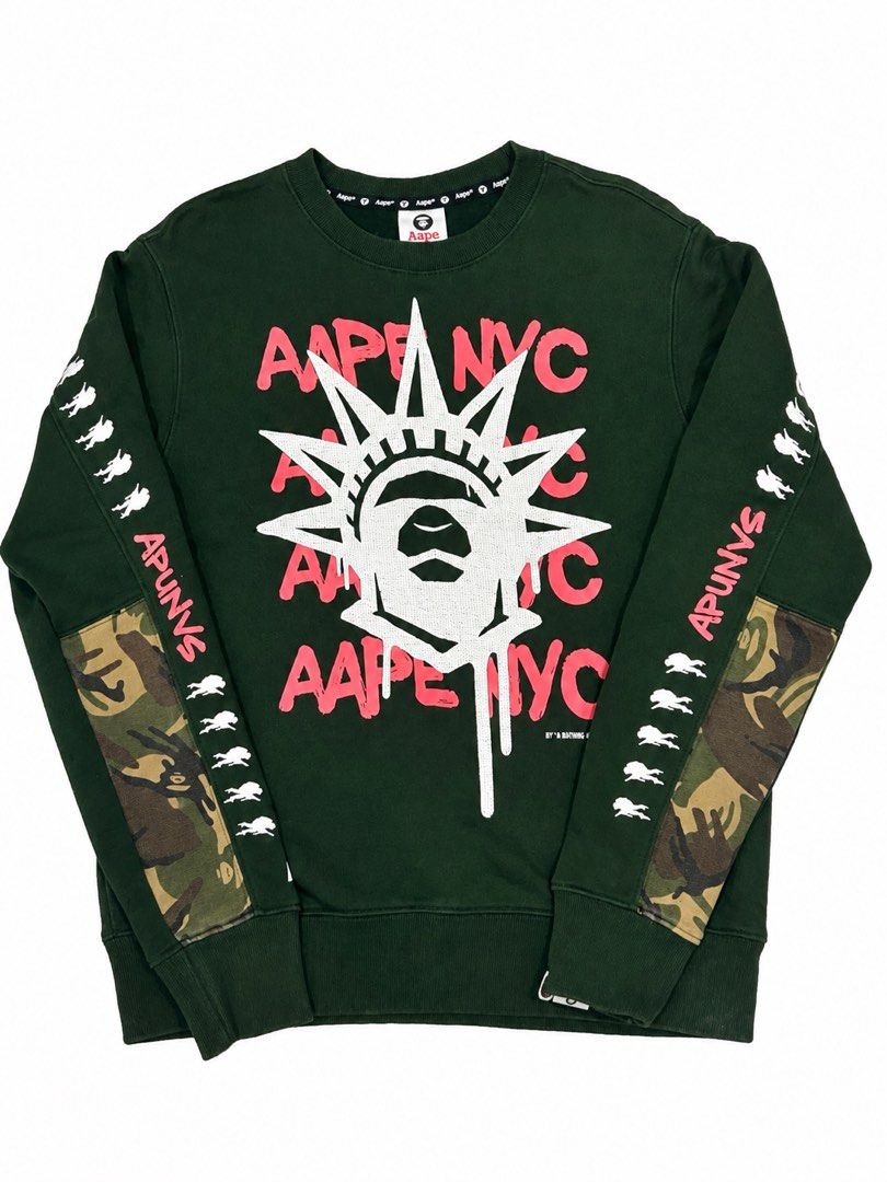 Aape By A Bathing Ape NYC Green Sweatshirt (Category: Coats, Jackets and Outerwear) located in Manila. Submitted by comeonthrift (Listing ID 1468465131, Image 1). Description: - Brand: Aape by A Bathing Ape - Color: Green - Size: Small - Design: Large white Statue of Liberty ape graphic with pink Aape NYC text on front - Details: Signature camo patches on both sleeves with small white graphics - Material: Comfortable cotton and polyester blend - 