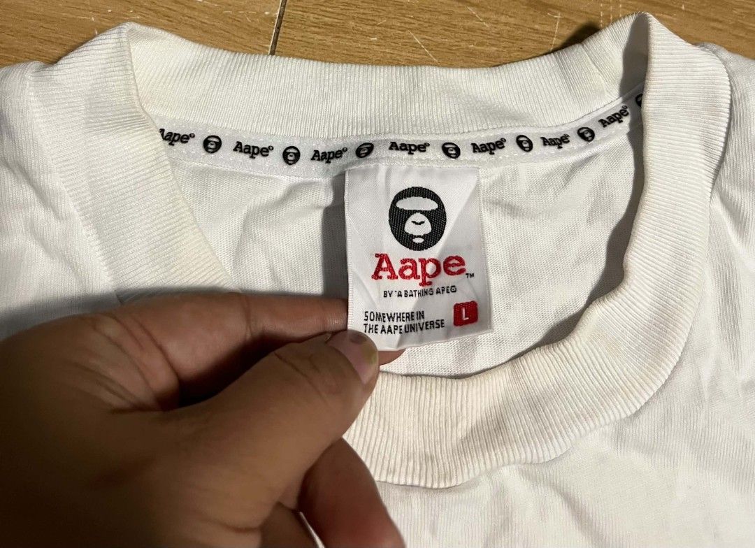 Aape By A Bathing Ape T-Shirt White Large (Category: Tshirts & Polo Shirts ) located in Compostela. Submitted by zackthrift07 (Listing ID 1468347948, Image 3). Description: - Brand: Aape by A Bathing Ape - Color: White with silver grey and black graphic - Size: Large - Material: 100% premium cotton - Design: Big Ape head logo on chest, signature repeating Aape inner tape, crew neck, short sleeves - Origin: Made in China - Condition: Brand new / E