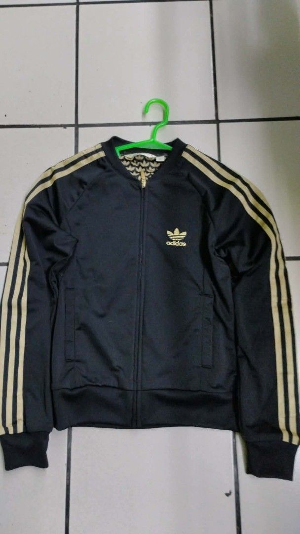 Adidas Black and Gold Track Jacket (Category: Coats, Jackets and Outerwear) located in Manila. Submitted by niggzreyno51476 (Listing ID 1468400312, Image 1). Description: - Brand: Adidas - Color: Black with gold details - Design: Classic 3-stripes on sleeves, small trefoil logo on chest, large embroidered trefoil logo on back - Lining: Patterned inner lining with repeating trefoil leaf print - Features: Zip-up front, side pockets, standard bomber