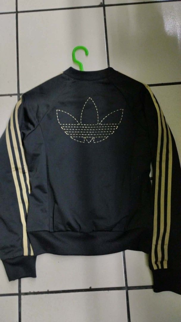 Adidas Black and Gold Track Jacket (Category: Coats, Jackets and Outerwear) located in Manila. Submitted by niggzreyno51476 (Listing ID 1468400312, Image 2). Description: - Brand: Adidas - Color: Black with gold details - Design: Classic 3-stripes on sleeves, small trefoil logo on chest, large embroidered trefoil logo on back - Lining: Patterned inner lining with repeating trefoil leaf print - Features: Zip-up front, side pockets, standard bomber