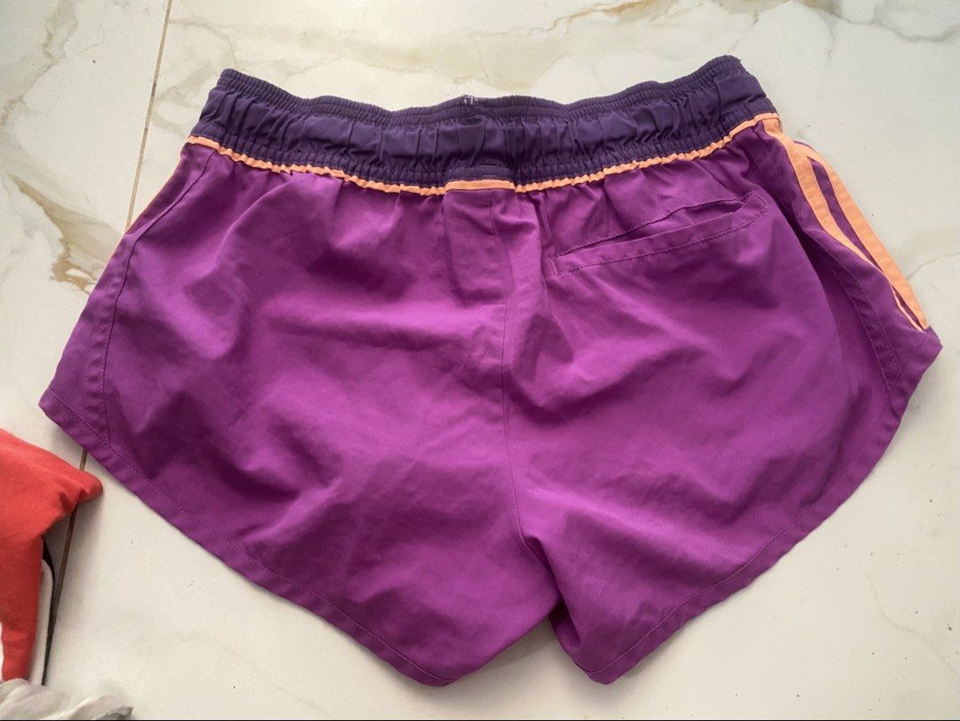 adidas running shorts (Category: Activewear) located in Mandaluyong City. Submitted by __chalai (Listing ID 1468363468, Image 2). Description: - Brand: Adidas - Size: Small - Color: Purple with orange side stripes and waistband - Material: Climalite fabric for moisture-wicking comfort - Features: Adjustable drawstring waist, embroidered silver Adidas logo, and a small back pocket with flap closure - Condition: Excellent.