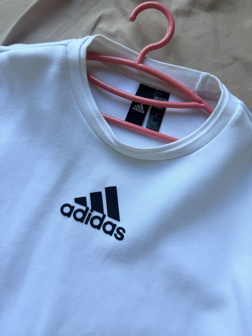 Adidas White Sweatshirt Size S (Category: Coats, Jackets and Outerwear) located in Manila. Submitted by lucipurrpreloved (Listing ID 1468333933, Image 2). Description: - Item: White Adidas crewneck sweatshirt - Size: Small - Design: Black Adidas logo on front chest - Unique Details: Side zipper near the hem and black rectangular text-print patch on lower back - Fit: Long sleeves with ribbed cuffs and collar - Condition: Brand new/Excellent (Ready