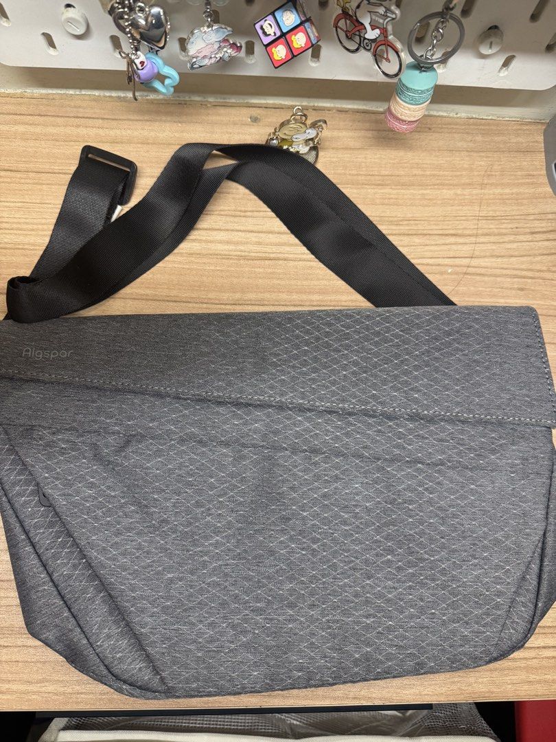Algspor Grey Crossbody Messenger Bag (Category: Sling Bags) located in Manila. Submitted by xenasales (Listing ID 1468375107, Image 1). Description: - Brand: Algspor - Color: Grey with navy blue lining - Design: Textured geometric pattern on front flap - Strap: Adjustable black nylon strap with buckle - Closure: Secure magnetic snap closure - Interior: Multiple slip and zip pockets for easy organization - Condition: Clean interior, ready for dail