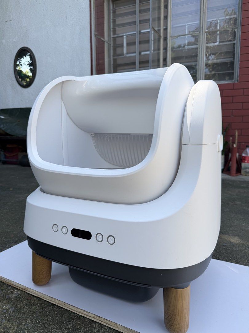 Automatic Smart Cat Litter Box Self-Cleaning (Category: Health & Grooming) located in Quezon City. Submitted by onlynina222 (Listing ID 1468341144, Image 1). Description: - Color: Clean white with stylish wooden legs - Design: Modern minimal look with a front control panel and easy-to-use power buttons - Interior: Gray inner lining with clear MIN and MAX fill level markers - Functionality: Built-in sifter grill for automatic waste management - Pe