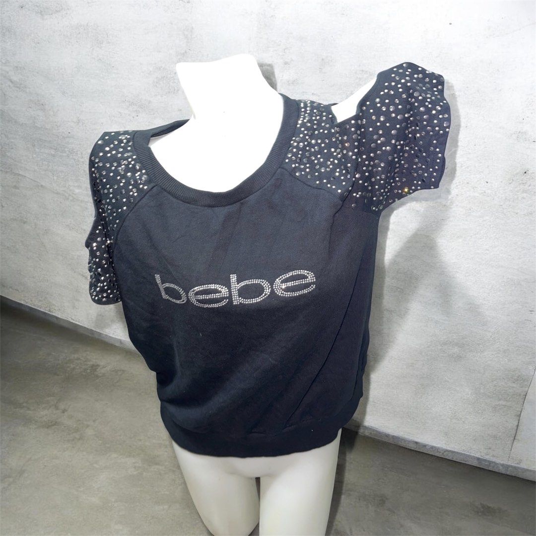 Bebe Black Rhinestone Embellished Cold Shoulder Sweater (Category: Longsleeves) located in Manila. Submitted by fastforest_65f95b (Listing ID 1468396169, Image 1). Description: - Brand: Bebe - Style: Black knit sweater with scoop neckline - Details: Trendy shoulder cutouts and sparkling rhinestones covering both sleeves - Branding: Iconic 'bebe' logo spelled out in rhinestones across the chest - Fit: Ribbed trim at the collar and hem for a comfor