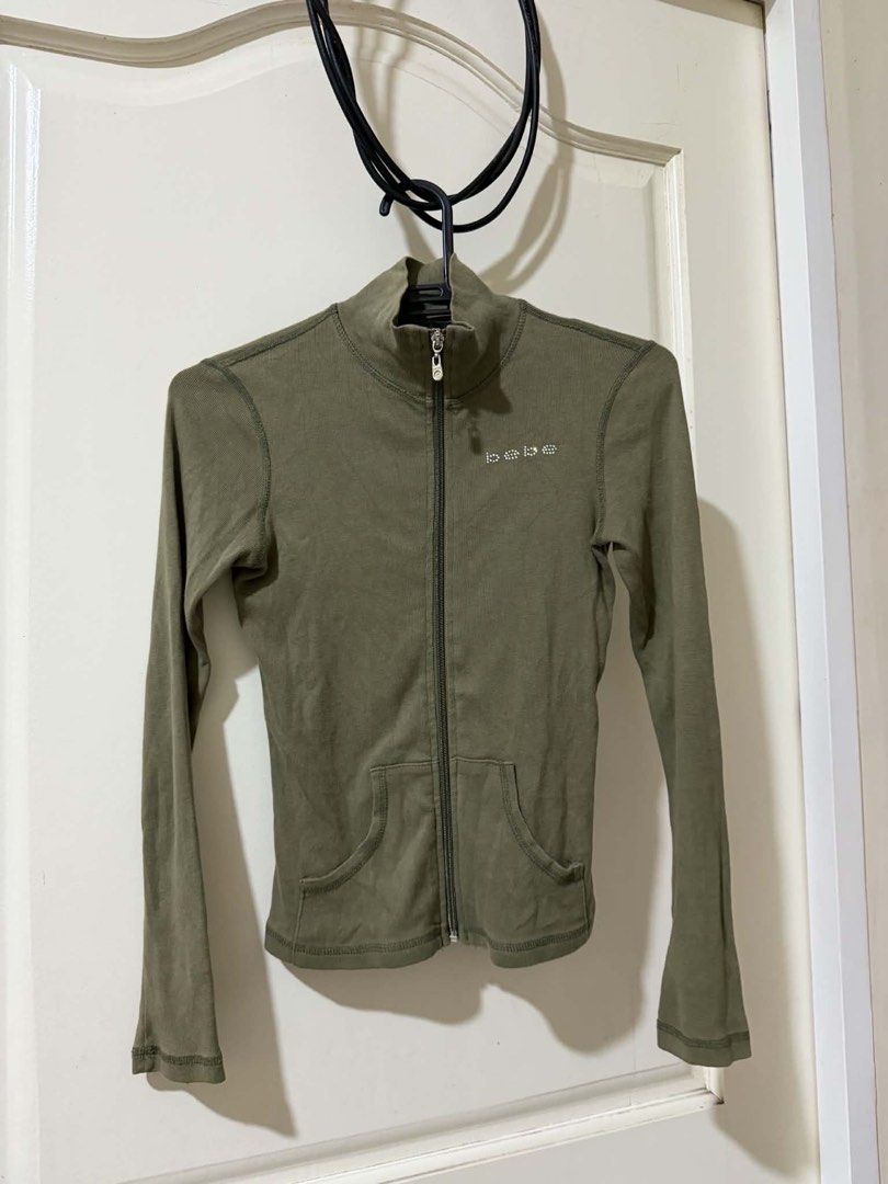 Bebe Olive Green Ribbed Zip-Up Jacket (Category: Coats, Jackets and Outerwear) located in Davao. Submitted by arbeepogio63169 (Listing ID 1468328236, Image 1). Description: - Brand: Bebe - Size: S (Made in U.S.A.) - Color: Olive green - Style: Fitted ribbed zip-up jacket with mock neck - Details: Signature rhinestone logo on left chest, branded metal zipper pull, and two front waist pockets - Condition: Excellent/Ready to wear.