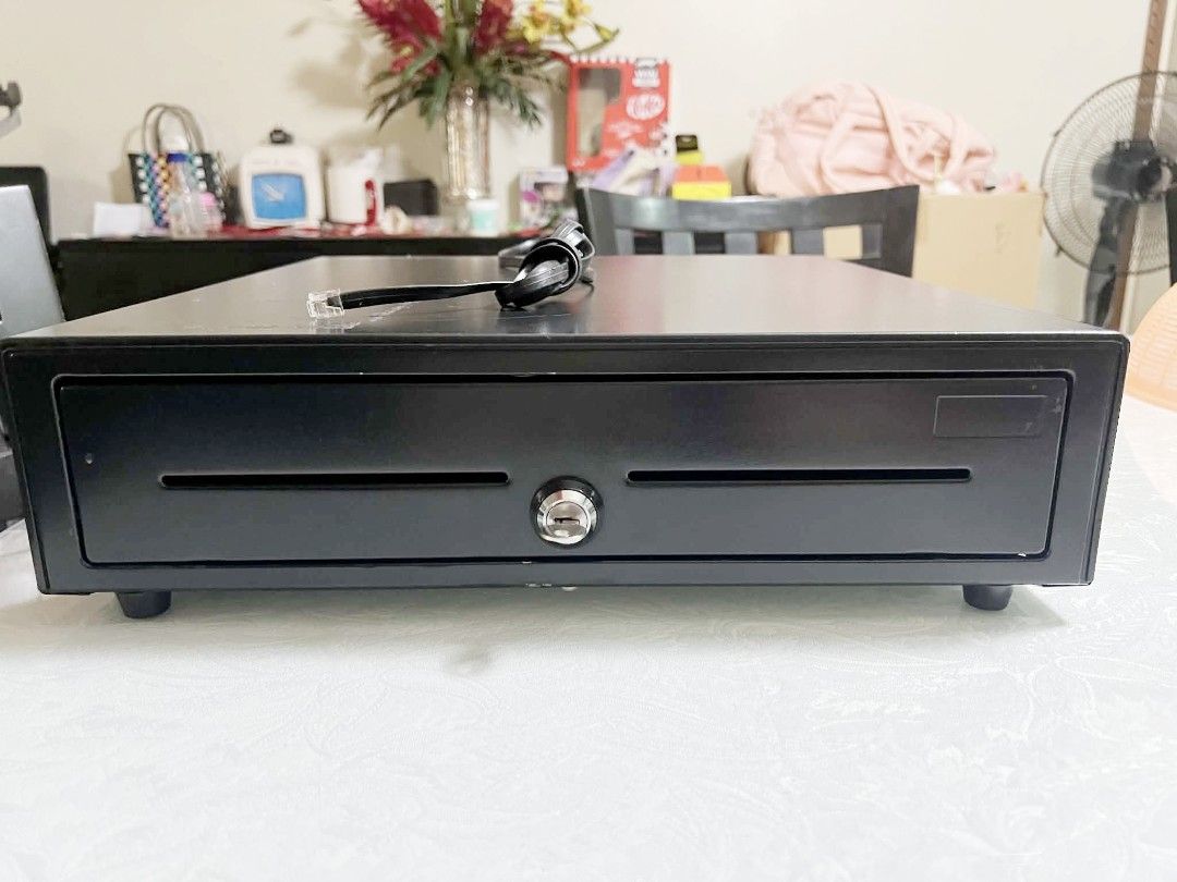 Black POS Cash Drawer with RJ11 Cable (Category: Office & Business Technology) located in Pasig City. Submitted by maming73 (Listing ID 1468305237, Image 2). Description: - Type: Sturdy black metal cash drawer for retail or office use - Features: Dual front media slots and a secure middle key lock - Connectivity: RJ11 cable attached at the top for receipt printer integration - Condition: Fully functional with minor scuffs on the top surface from 