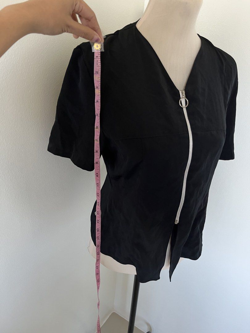 Black short-sleeve top with silver ring zipper (Category: Blouses) located in Mandaluyong City. Submitted by bravedeer.020ad7 (Listing ID 1468364820, Image 3). Description: - Color: Black - Style: Short-sleeve blouse with V-neck and front zipper - Accent: Trendy silver ring pull - Fit: Structured cut - Size/Measurements: Approx. 14 inches across the chest, 22 inches in length - Condition: Clean fabric, excellent overall condition.
