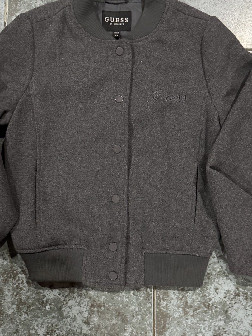 Bomber Jacket (Category: Coats, Jackets and Outerwear) located in Muntinlupa City. Submitted by avampaya (Listing ID 1468345802, Image 3). Description: - Brand: Guess - Color: Dark grey - Size: XS (can fit up to Small) - Closure: Snap button front - Details: Ribbed collar, cuffs, and hem, subtle embroidered logo on left chest, two side pockets - Just washed but never used.