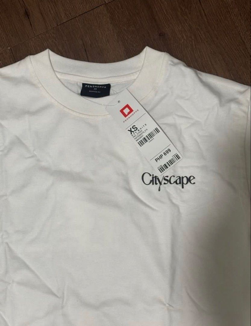 Brand new Penshoppe shirt (Category: Shirts) located in Subic. Submitted by declutterbyshit (Listing ID 1468306945, Image 1). Description: - Brand: Penshoppe - Style: Cityscape t-shirt - Color: White - Size: XS (27x20) fits to med (fits big) - Details: Short sleeves, classic crew neck, small front chest print, and large colorful city graphic with text on the back - Condition: Brand new with original store tag still attached.