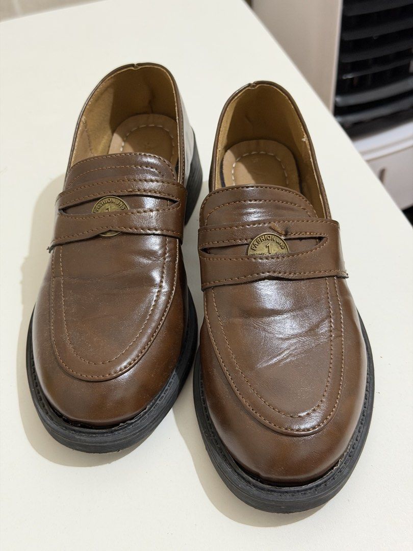 Brown Penny Loafers with Decorative Coin Strap (Category: Loafers) located in Taguig. Submitted by deguzmanke83356 (Listing ID 1468326331, Image 3). Description: - Color & Material: Dark brown faux leather - Minimal Flaw: Glue comes off - Style: Slip-on penny loafers with a decorative metallic coin strap - Sole: Chunky black lug sole with a low block heel - Usage: Versatile casual everyday footwear - Condition: Minor sole separation near the fron