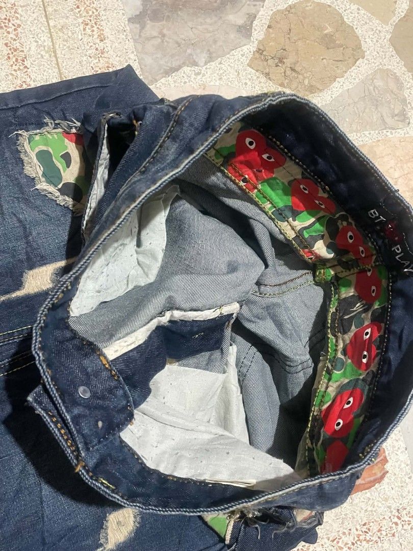 BT Play Denim Jeans with Camo Patchwork (Category: Jeans) located in Manila. Submitted by gentlecloud_713dbd (Listing ID 1468457106, Image 3). Description: - Brand: BT Play (Tag still attached) - Wash: Dark wash denim - Style: Distressed with green camo patchwork and red heart graphics - Details: Multi-pocket design, raw edge hems, button closure - Interior: Camo print waistband lined with red heart motifs.