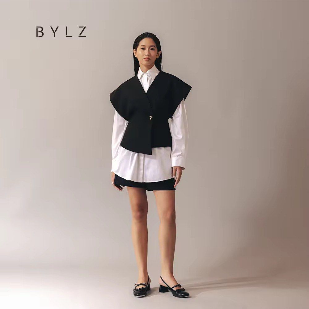 BYLZ Black Textured Asymmetric Vest (Category: Sleeveless) located in Makati City. Submitted by anndeetree (Listing ID 1468368220, Image 1). Description: - Brand: BYLZ - Color: Dark charcoal black - Material: Lightweight textured woven fabric with clean inner lining - Design: V-neckline, short sleeves, and structured shoulders - Closure & Hem: Asymmetrical front hem with a gold-tone triangle button - Condition: Excellent, collar tag intact - Styl