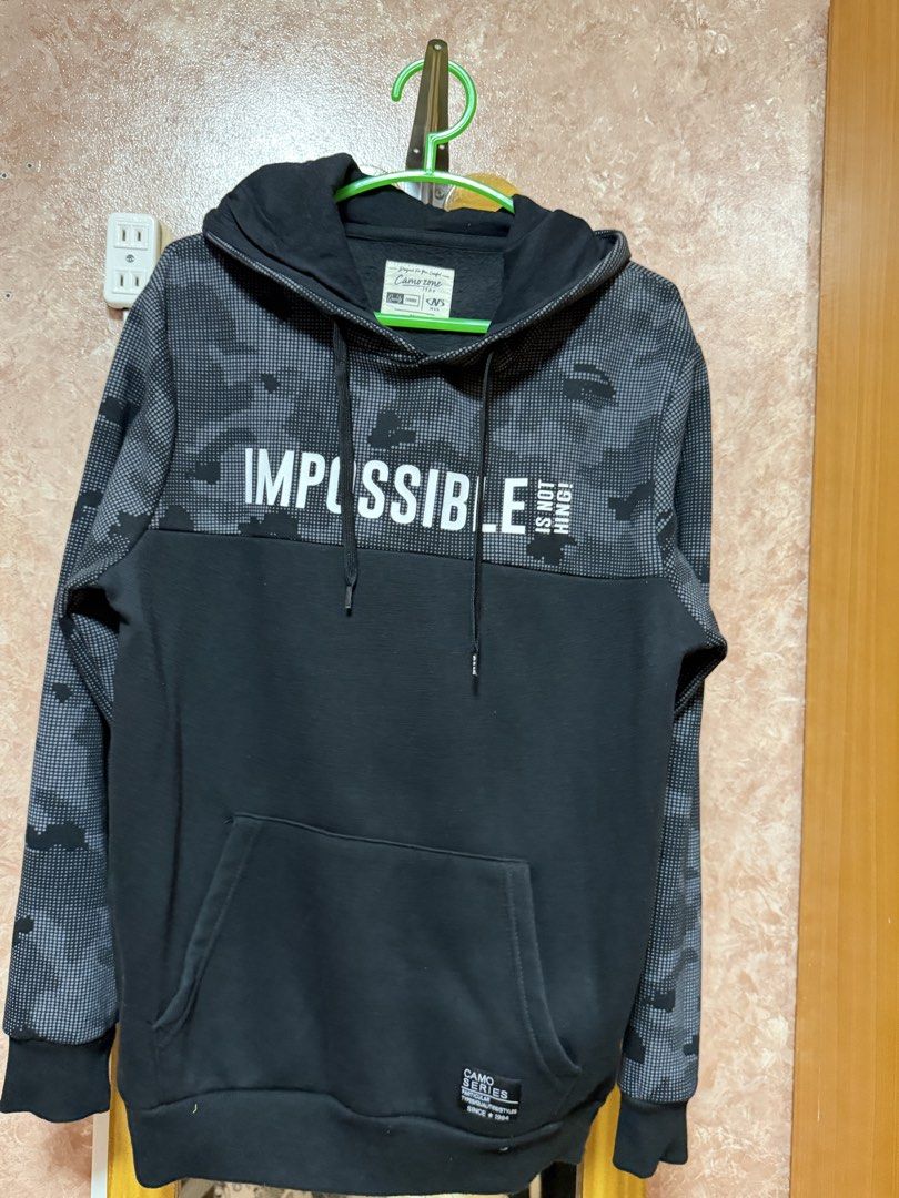 Camo Zone Impossible Is Nothing Black Hoodie (Category: Hoodies) located in Bacoor. Submitted by happyfish_028a6c (Listing ID 1468495055, Image 1). Description: - Brand/Model: Camo Zone Black Hoodie - Design: Grey pixel camouflage on upper chest, sleeves, and hood with bold white 'IMPOSSIBLE IS NOTHING' chest print - Features: Front kangaroo pocket, adjustable hood drawstrings, and 'Camo Series' woven hem patch - Style: Casual streetwear, comfort