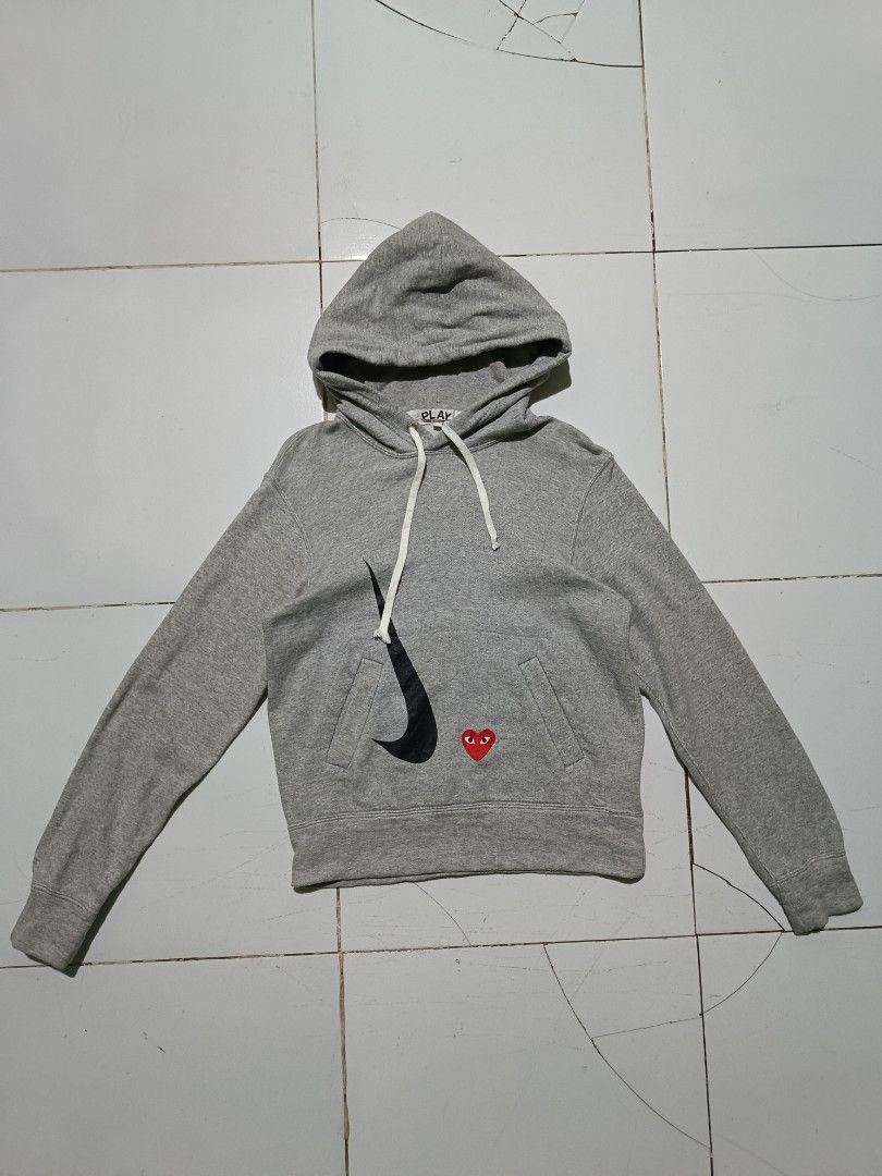 CDG PLAY x Nike Grey Pullover Hoodie (Category: Coats, Jackets and Outerwear) located in Barotac Nuevo. Submitted by gray101 (Listing ID 1468406723, Image 1). Description: - Brand: Comme des Garçons Play x Nike - Color: Grey - Size/Condition: Clean piece, worn only a few times - Design: Embroidered red heart logo near the front pocket - Graphics: Black swoosh graphic printed on the lower front - Features: Drawstring hood with white cords, kangaro