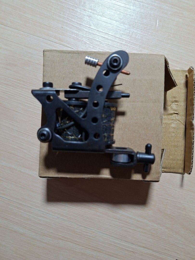 Coil Tattoo Machine Black and Gold (Category: Craft Supplies & Tools) located in Baguio. Submitted by restyrille77846 (Listing ID 1468313817, Image 1). Description: - Color: Black and gold with patterned coil wraps - Setup: Standard setup with binding posts and contact screw - Condition: Brand new, never used, kept in storage - Inclusions: Comes with original cardboard box.