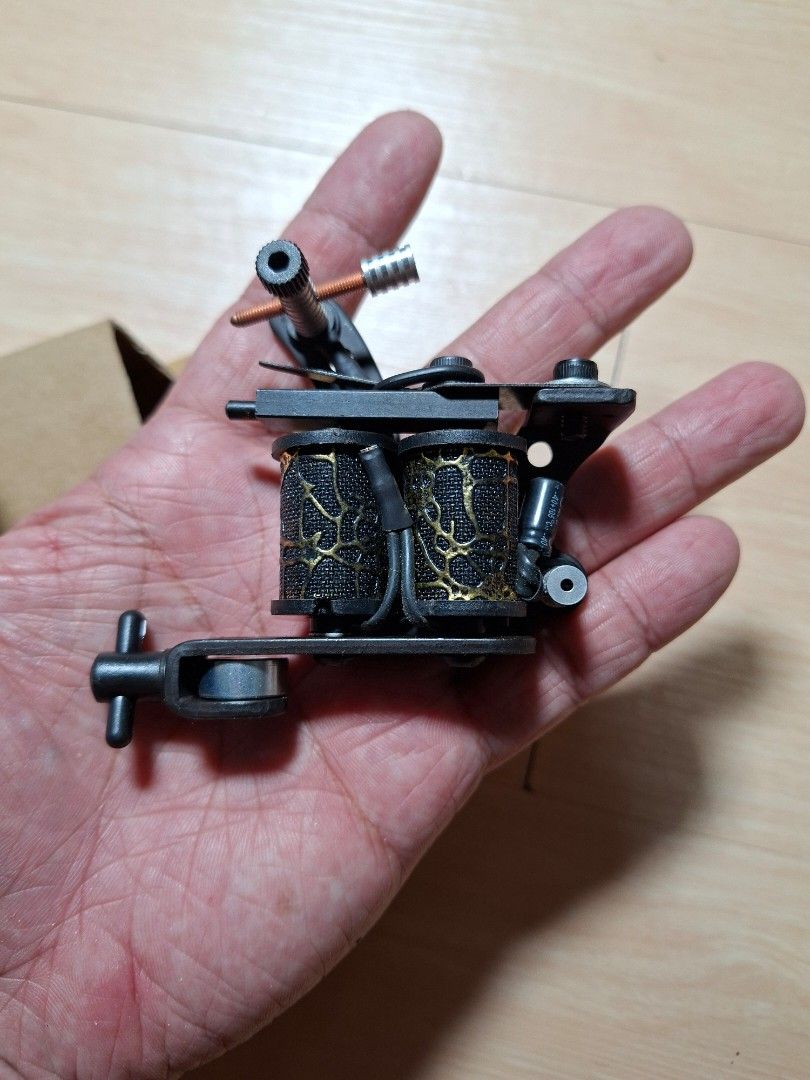 Coil Tattoo Machine Black and Gold (Category: Craft Supplies & Tools) located in Baguio. Submitted by restyrille77846 (Listing ID 1468313817, Image 2). Description: - Color: Black and gold with patterned coil wraps - Setup: Standard setup with binding posts and contact screw - Condition: Brand new, never used, kept in storage - Inclusions: Comes with original cardboard box.