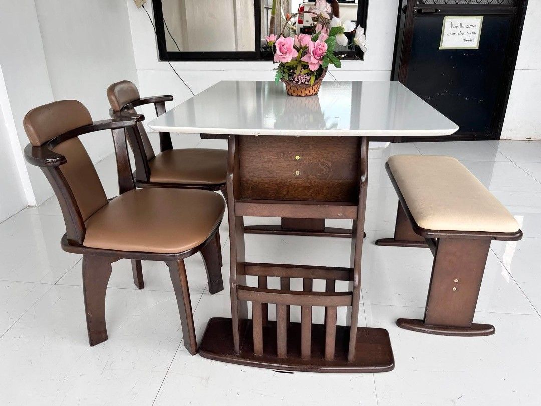 Dining table set with chairs and storage base (Category: Tables & Sets) located in Manila. Submitted by roveeeeelen_06 (Listing ID 1468300013, Image 1). Description: - Dark wood dining set - White table top with convenient drop-down sides - Built-in vertical slots underneath for books or magazines - Includes 2 chairs with comfortable brown cushions - Includes 1 matching bench seat with a beige pad - Sturdy and durable frame throughout.