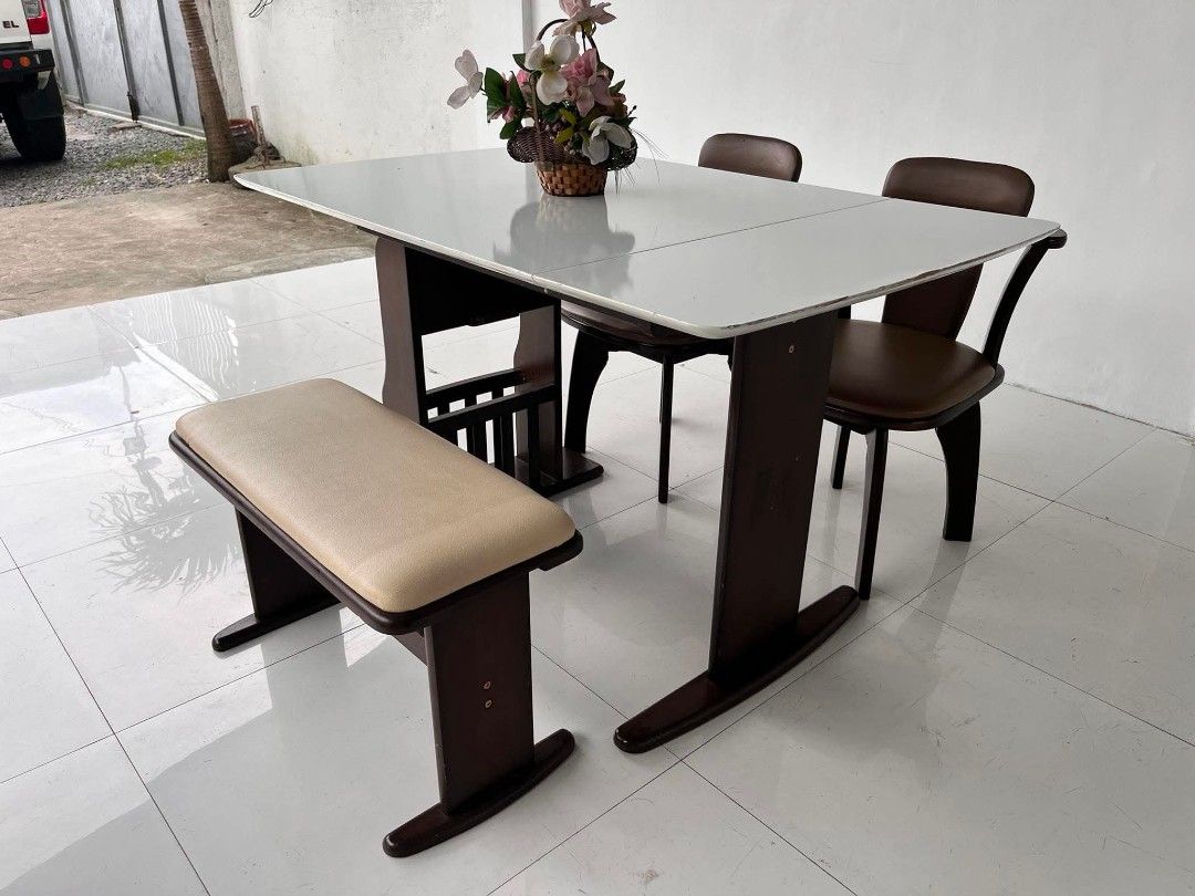 Dining table set with chairs and storage base (Category: Tables & Sets) located in Manila. Submitted by roveeeeelen_06 (Listing ID 1468300013, Image 3). Description: - Dark wood dining set - White table top with convenient drop-down sides - Built-in vertical slots underneath for books or magazines - Includes 2 chairs with comfortable brown cushions - Includes 1 matching bench seat with a beige pad - Sturdy and durable frame throughout.