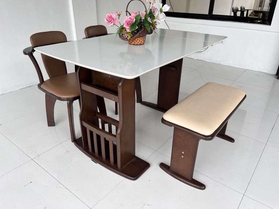 Dining table set with chairs and storage base (Category: Tables & Sets) located in Manila. Submitted by roveeeeelen_06 (Listing ID 1468300013, Image 2). Description: - Dark wood dining set - White table top with convenient drop-down sides - Built-in vertical slots underneath for books or magazines - Includes 2 chairs with comfortable brown cushions - Includes 1 matching bench seat with a beige pad - Sturdy and durable frame throughout.