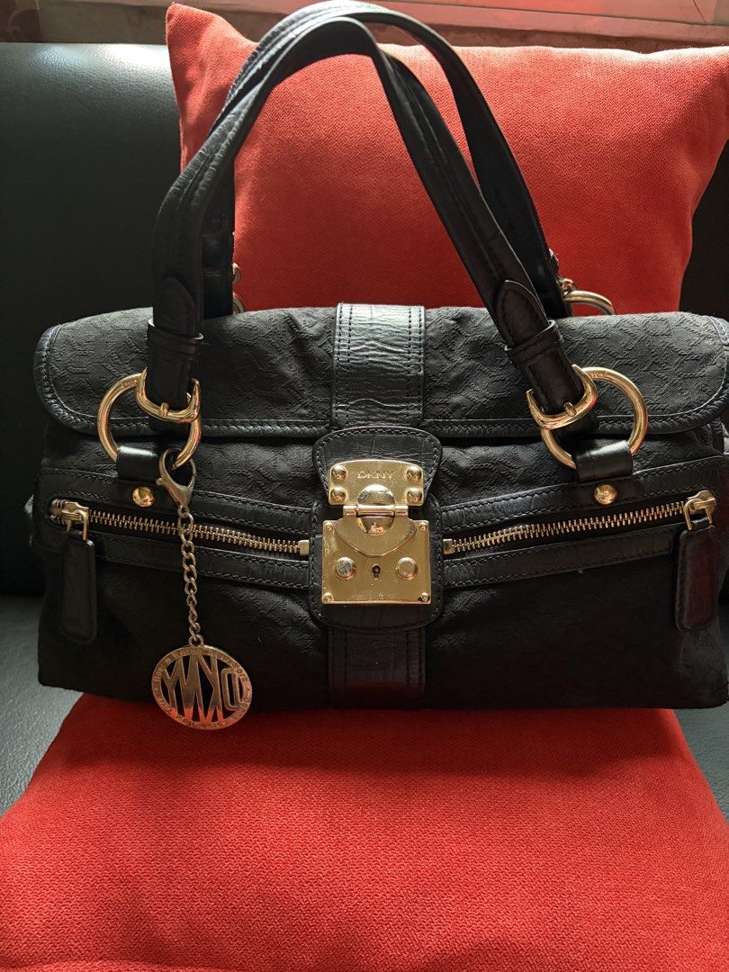 DKNY Black Structured Handbag with Gold Hardware (Category: Luxury Bags & Wallets) located in Caloocan City. Submitted by wildstar.f2ca8a (Listing ID 1468499347, Image 1). Description: Classic black handbag from DKNY. Sturdy top handles, gold-tone hardware, and a secure lock closure on the front flap. Includes dual zippered pockets below the flap for easy access. Hanging logo charm attached to the ring. Clean fabric interior with plenty of room f