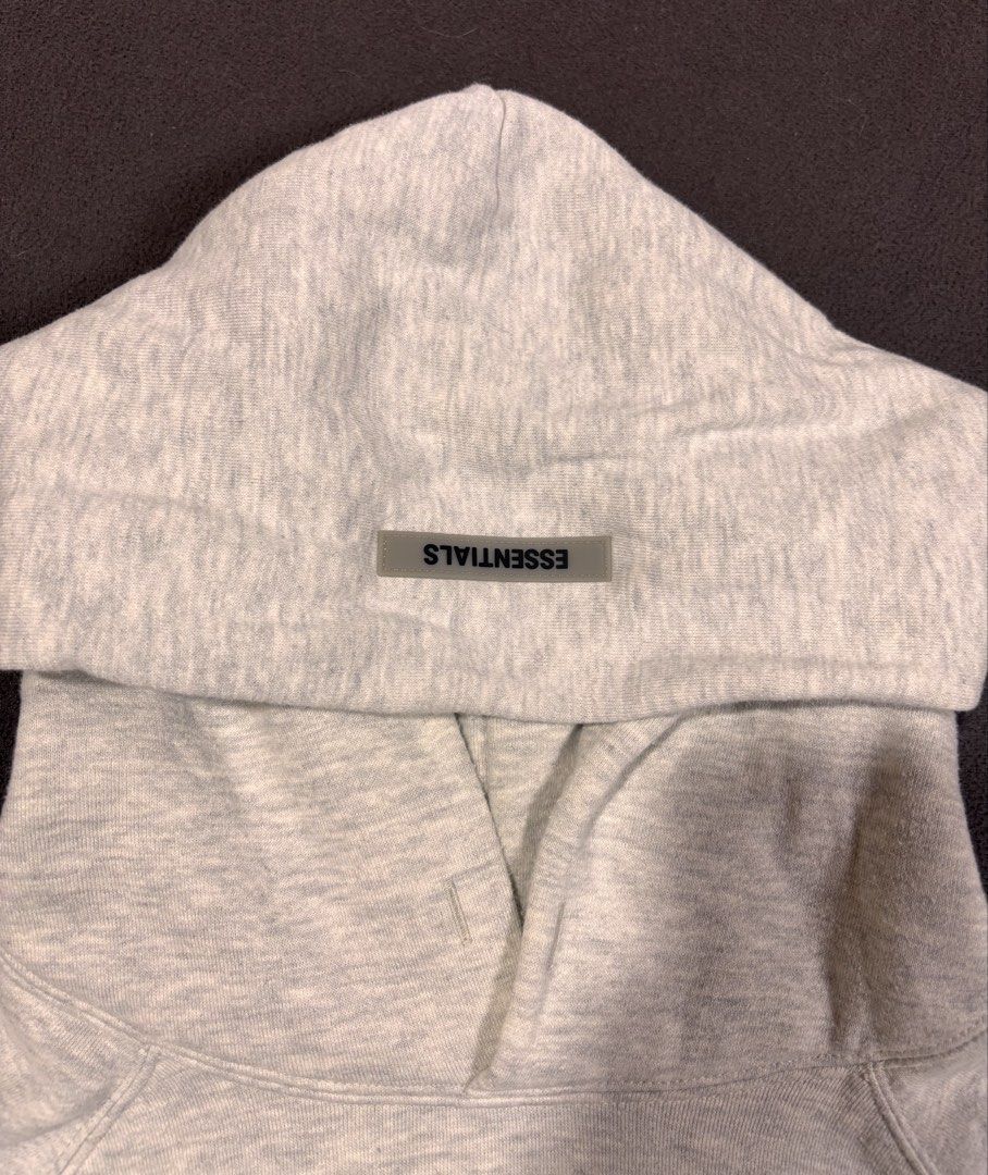 Essentials Grey pull over hoodie (Category: Hoodies) located in Mabalacat. Submitted by _limitlessfashion (Listing ID 1468299357, Image 3). Description: - Brand/Model: Fear of God Essentials Hoodie - Color: Light Grey Melange - Size medium on tag - Length 27 - Width 26.5 - Color rate 9.5 - Issue minimal washable yellow stain - Fit: Classic oversized fit - Details: Black chest branding, rubberized hood patch, sleeve text print, and kangaroo pocket