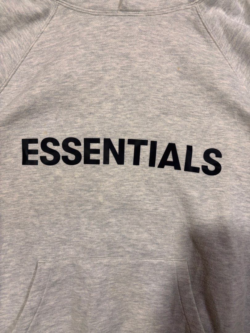Essentials Grey pull over hoodie (Category: Hoodies) located in Mabalacat. Submitted by _limitlessfashion (Listing ID 1468299357, Image 2). Description: - Brand/Model: Fear of God Essentials Hoodie - Color: Light Grey Melange - Size medium on tag - Length 27 - Width 26.5 - Color rate 9.5 - Issue minimal washable yellow stain - Fit: Classic oversized fit - Details: Black chest branding, rubberized hood patch, sleeve text print, and kangaroo pocket
