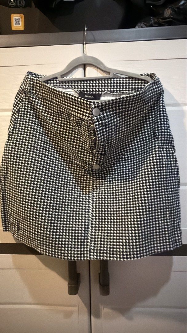 Forever 21 Black And White Houndstooth Mini Skirt (Category: Skirts) located in Manila. Submitted by adoptmypreloveditems (Listing ID 1468477319, Image 1). Description: - Brand: Forever 21 - Style: High-waisted mini skirt with a structured fit - Pattern: Timeless black and white houndstooth - Details: Front row of silver metal buttons, clean inside tag - Material: Textured fabric - Condition: Excellent, ready to wear - Styling: Pairs effortlessly