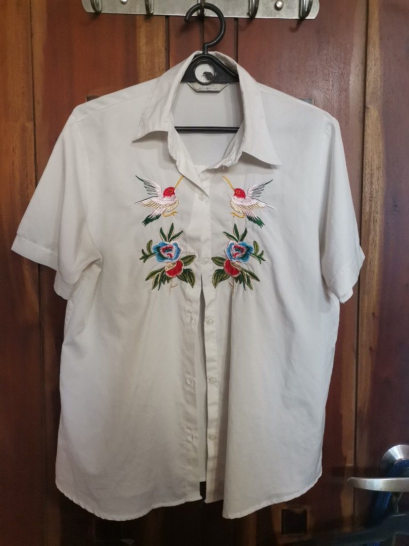 GRACE White Embroidered Short Sleeve Button-Down Shirt (Category: Shirts) located in Makati City. Submitted by kookybearsstuff (Listing ID 1468348584, Image 1). Description: - Brand: GRACE - Style: Short sleeve button-down shirt with standard collar and front button closure - Design: Stunning, colorful floral and hummingbird embroidery on the chest - Details: Chic pleat detail on the back - Material: Lightweight and comfortable fabric - Versatili