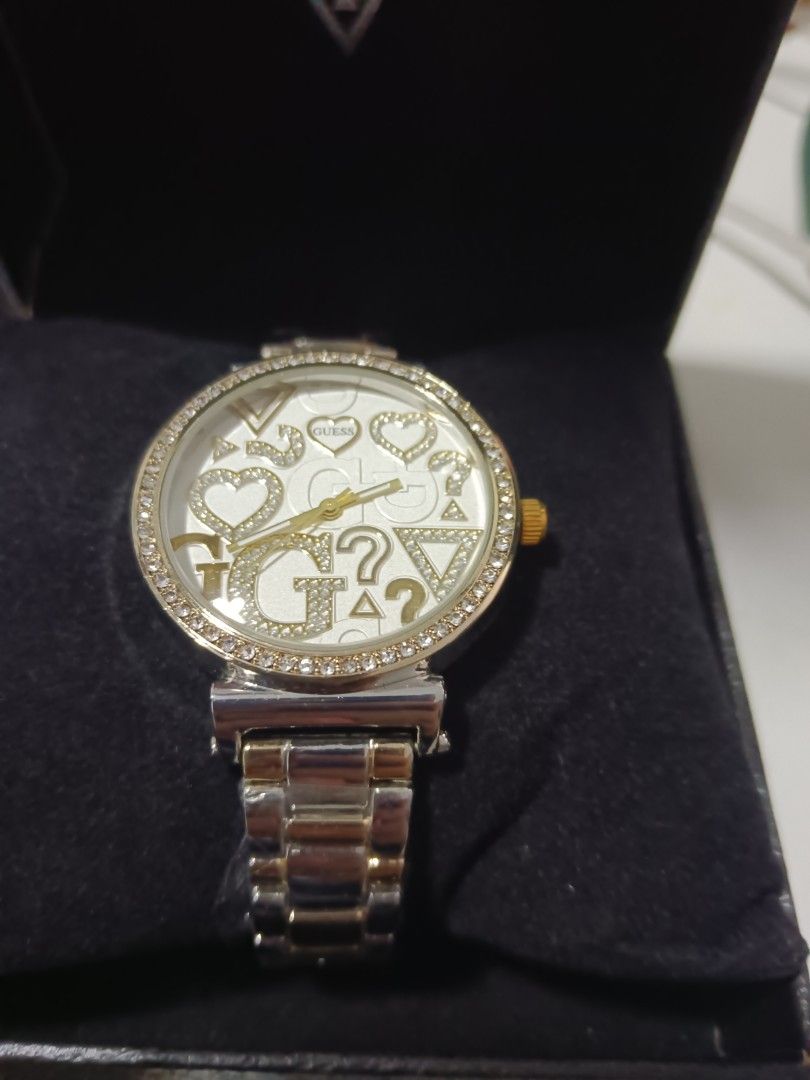 Guess Rhinestone Dial Two-Tone Watch with Box (Category: Women's Watches) located in Tarlac. Submitted by clover_co. (Listing ID 1468337255, Image 2). Description: Guess analog watch featuring a two-tone silver and gold stainless steel bracelet. Round white dial covered with crystal rhinestone embellishments, brand logos, hearts, and triangles. Gold-tone hands and crown. Crystal stones embedded around the bezel. Comes in a black presentation box.