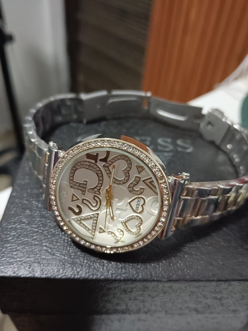Guess Rhinestone Dial Two-Tone Watch with Box (Category: Women's Watches) located in Tarlac. Submitted by clover_co. (Listing ID 1468337255, Image 3). Description: Guess analog watch featuring a two-tone silver and gold stainless steel bracelet. Round white dial covered with crystal rhinestone embellishments, brand logos, hearts, and triangles. Gold-tone hands and crown. Crystal stones embedded around the bezel. Comes in a black presentation box.