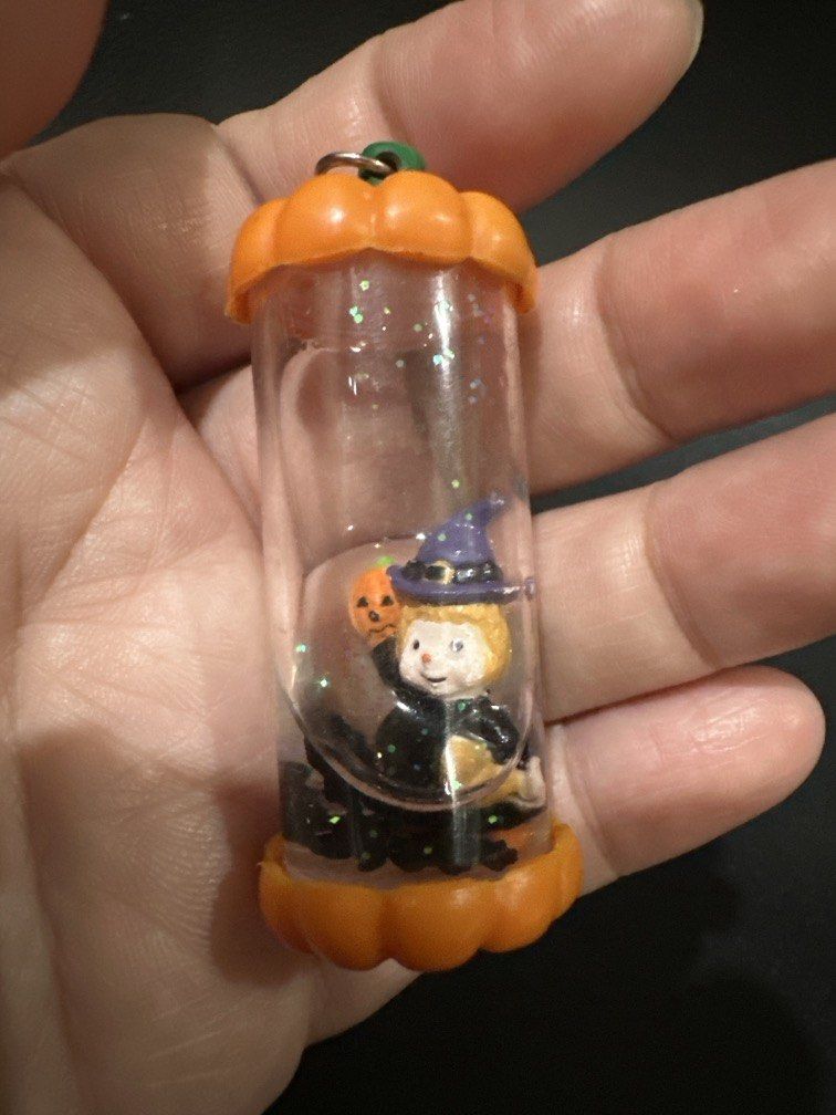 Halloween-themed water globe Keychain (Category: Everything Else Others) located in Manila. Submitted by krystalchewey_ (Listing ID 1468318138, Image 3). Description: Bnew Actual Photo Posted 180php featuring a witch and a pumpkin inside a clear cylinder capped with orange pumpkin-shaped ends.