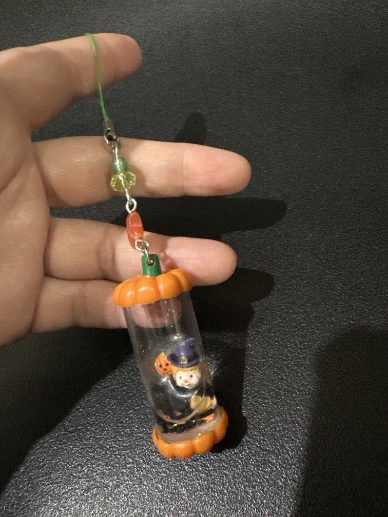 Halloween-themed water globe Keychain (Category: Everything Else Others) located in Manila. Submitted by krystalchewey_ (Listing ID 1468318138, Image 2). Description: Bnew Actual Photo Posted 180php featuring a witch and a pumpkin inside a clear cylinder capped with orange pumpkin-shaped ends.