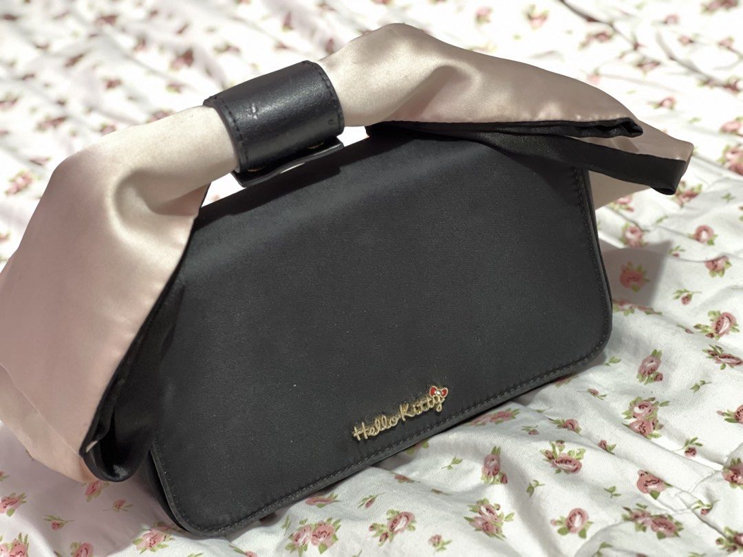 Hello Kitty Black hand Bag with Satin Bow Handle (sling strap missing) (Category: Shoulder Bags) located in Pasig City. Submitted by morilove (Listing ID 1468304827, Image 1). Description: - Brand: Kitty - Color: Black with a pink and black satin bow - Material: Structured design with fabric lining - Hardware: Gold metal logo lettering on front flap - Closure: Secure magnetic snap - Interior: Includes a woven Kitty label patch inside the pocket -