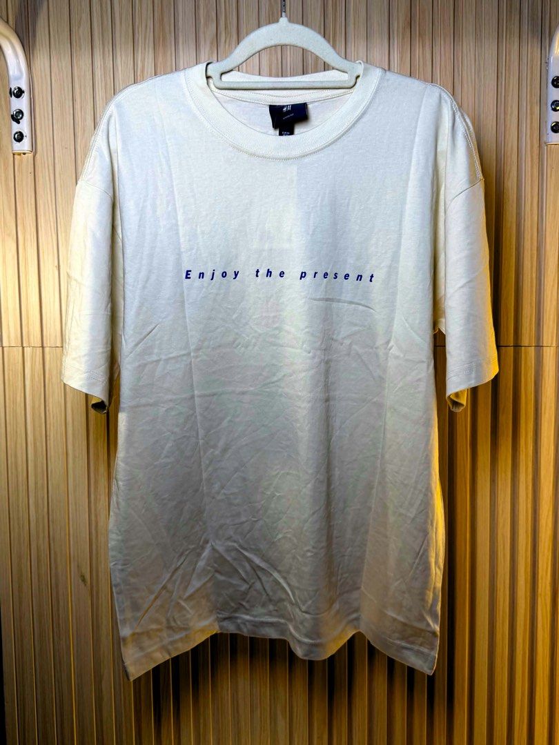 H&M Move Slower Graphic T-Shirt (Category: Tshirts & Polo Shirts ) located in Valenzuela. Submitted by luckyfalcon_011a05 (Listing ID 1468479458, Image 2). Description: - Brand: H&M - Color: Off-white - Size: Small - Fit: Loose fit with dropped shoulders and short sleeves - Design: Small 'Enjoy the present' text on the chest; bold 'MOVE SLOWER' graphic on the back - Condition: Excellent, clean with no stains or damage.